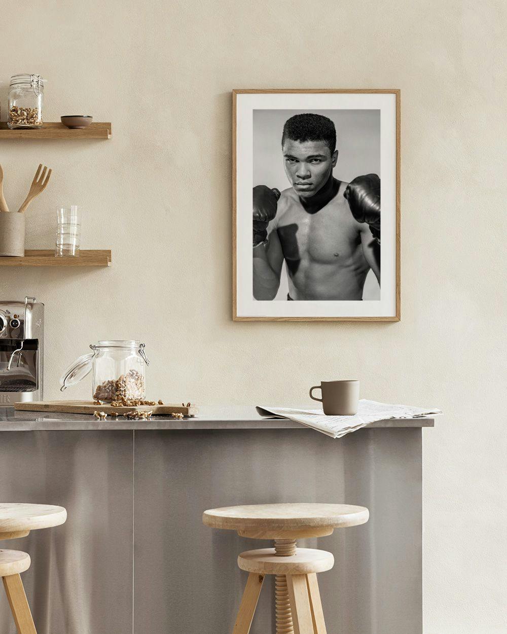 Affiche en noir et blanc de Mohamed Ali en boxeur, suspendue dans un salon moderne au-dessus dun fauteuil.