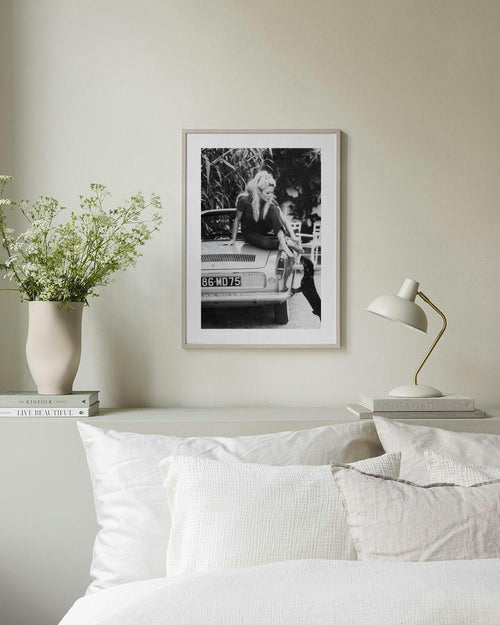 Affiche en noir et blanc de Brigitte Bardot assise sur une voiture, accrochée au mur dans un salon moderne.