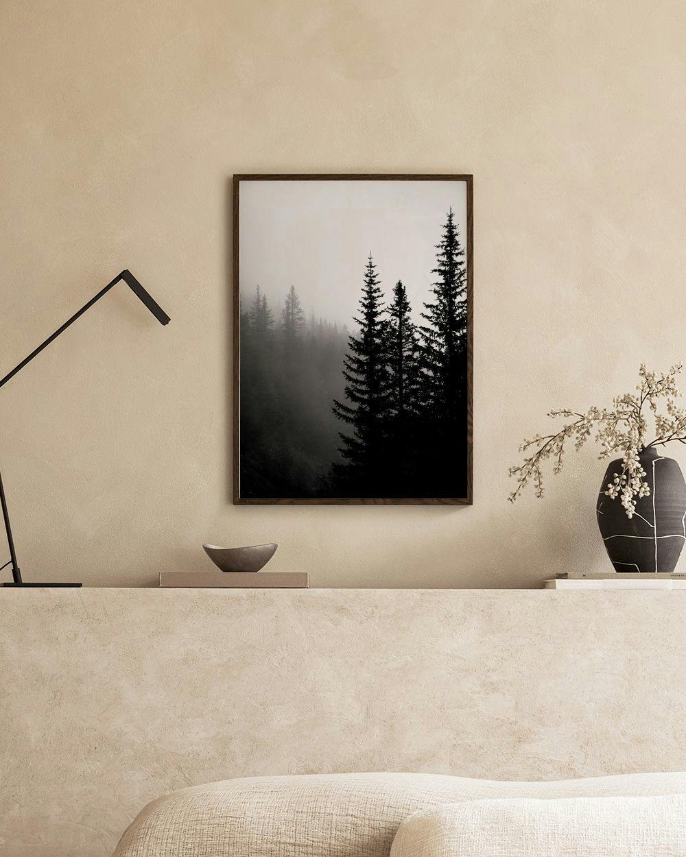 Affiche noire et blanche de sapins dans le brouillard, suspendue dans un salon moderne au-dessus dun meuble bas.