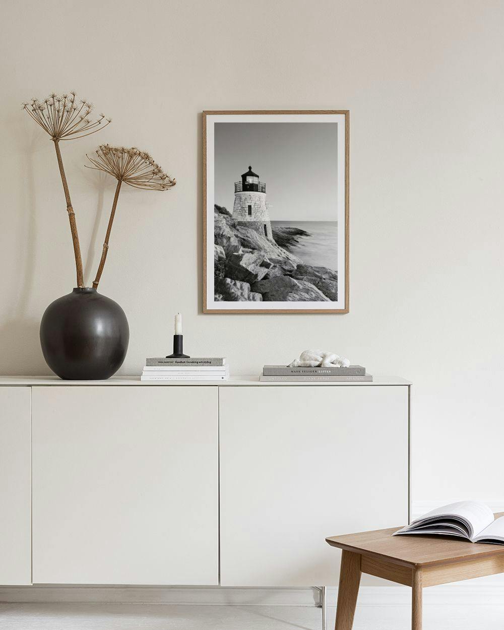 Affiche en noir et blanc dun phare sur des rochers au bord de la mer, posée sur une console grise.