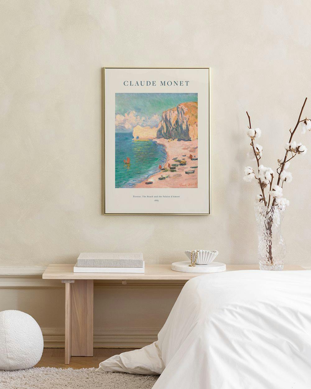 Affiche Claude Monet de la plage dÉtretat, avec falaises et bateaux, accrochée au-dessus dune table de chevet.