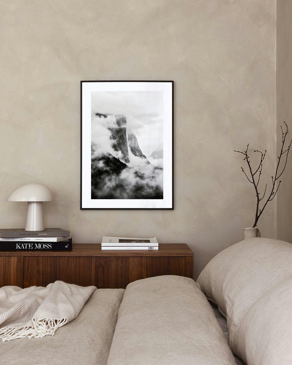 Affiche en noir et blanc dun paysage montagneux brumeux, accrochée au mur dans un salon moderne avec pouf et table basse.