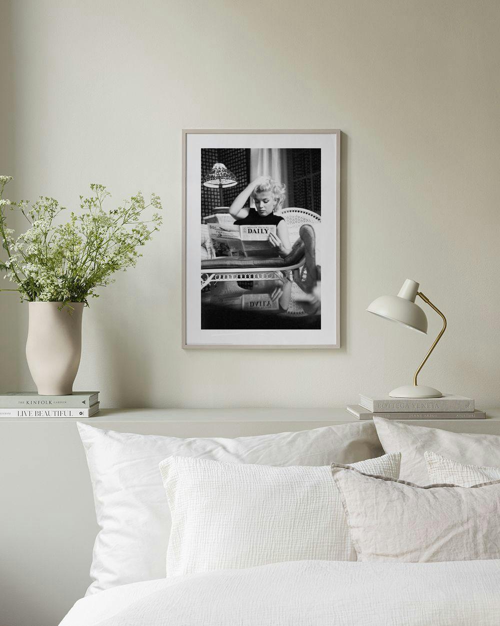 Affiche en noir et blanc de Marilyn Monroe lisant un journal, accrochée au-dessus dune console noire avec un vase et des livres.