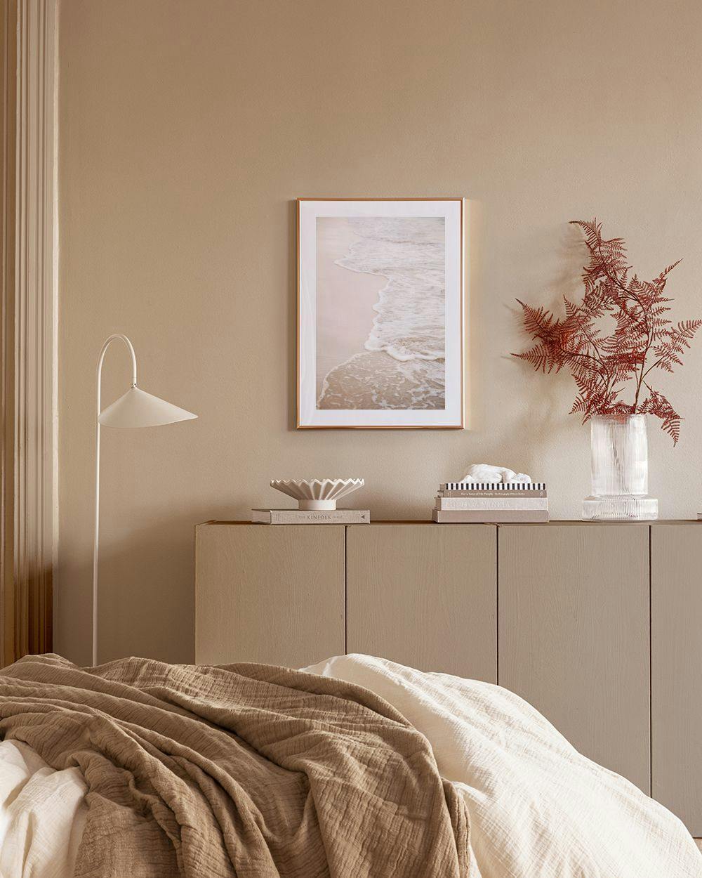 Affiche avec une plage de sable beige et des vagues écumeuses, accrochée dans une chambre moderne près dune plante.