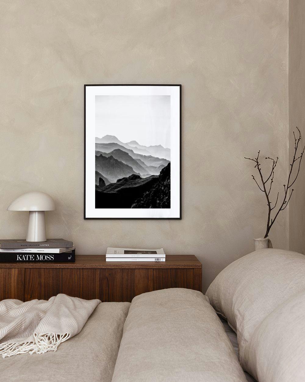 Affiche noir et blanc de montagnes brumeuses, exposée au-dessus dun meuble blanc avec un vase gris et une chaise bleue.