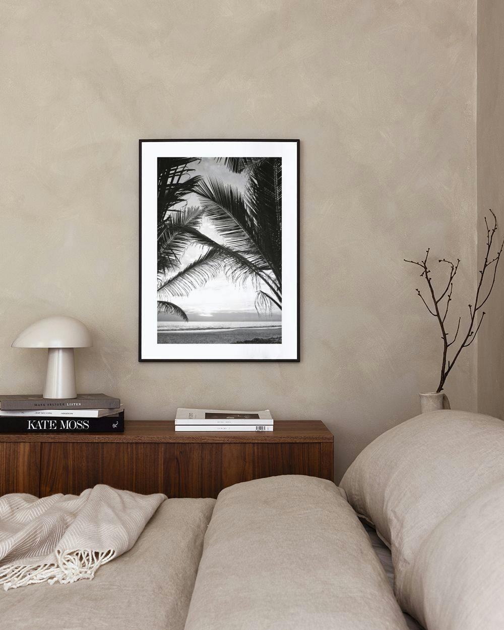 Affiche noir et blanc de palmiers et dune plage au coucher du soleil, accrochée au-dessus dune table basse avec vase.