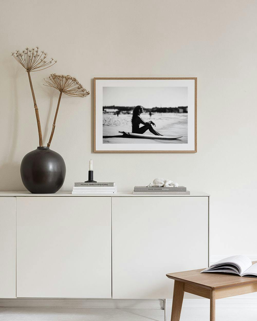 Affiche noir et blanc dune surfeuse assise sur sa planche, dans un salon moderne.