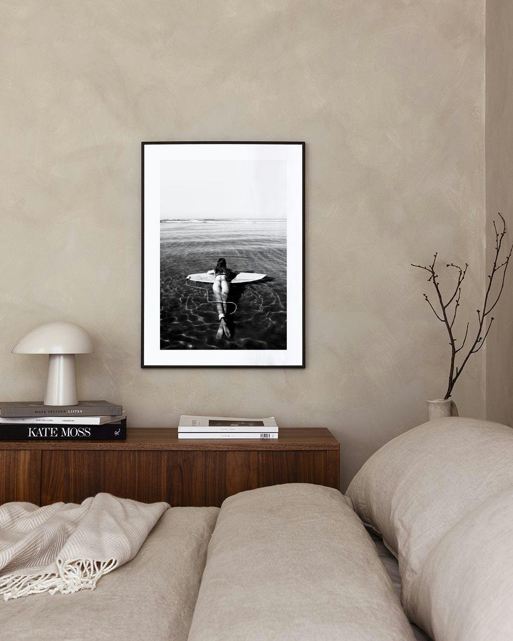Affiche noir et blanc dune surfeuse sur sa planche dans leau, suspendue au-dessus dun bureau en bois.