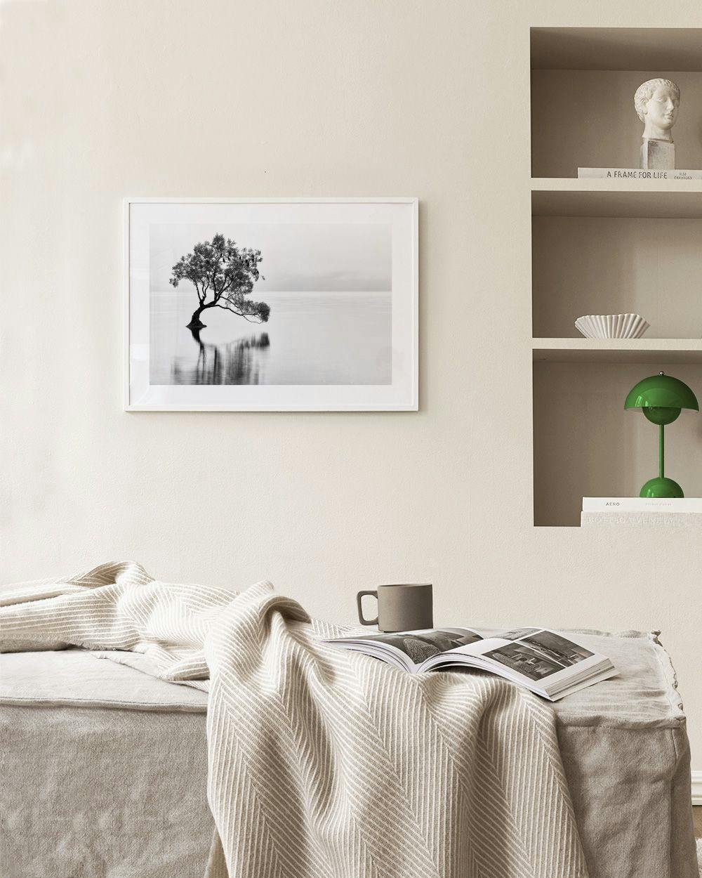 Affiche noir et blanc dun arbre solitaire dans leau, suspendue au-dessus dun fauteuil vert dans un salon moderne.