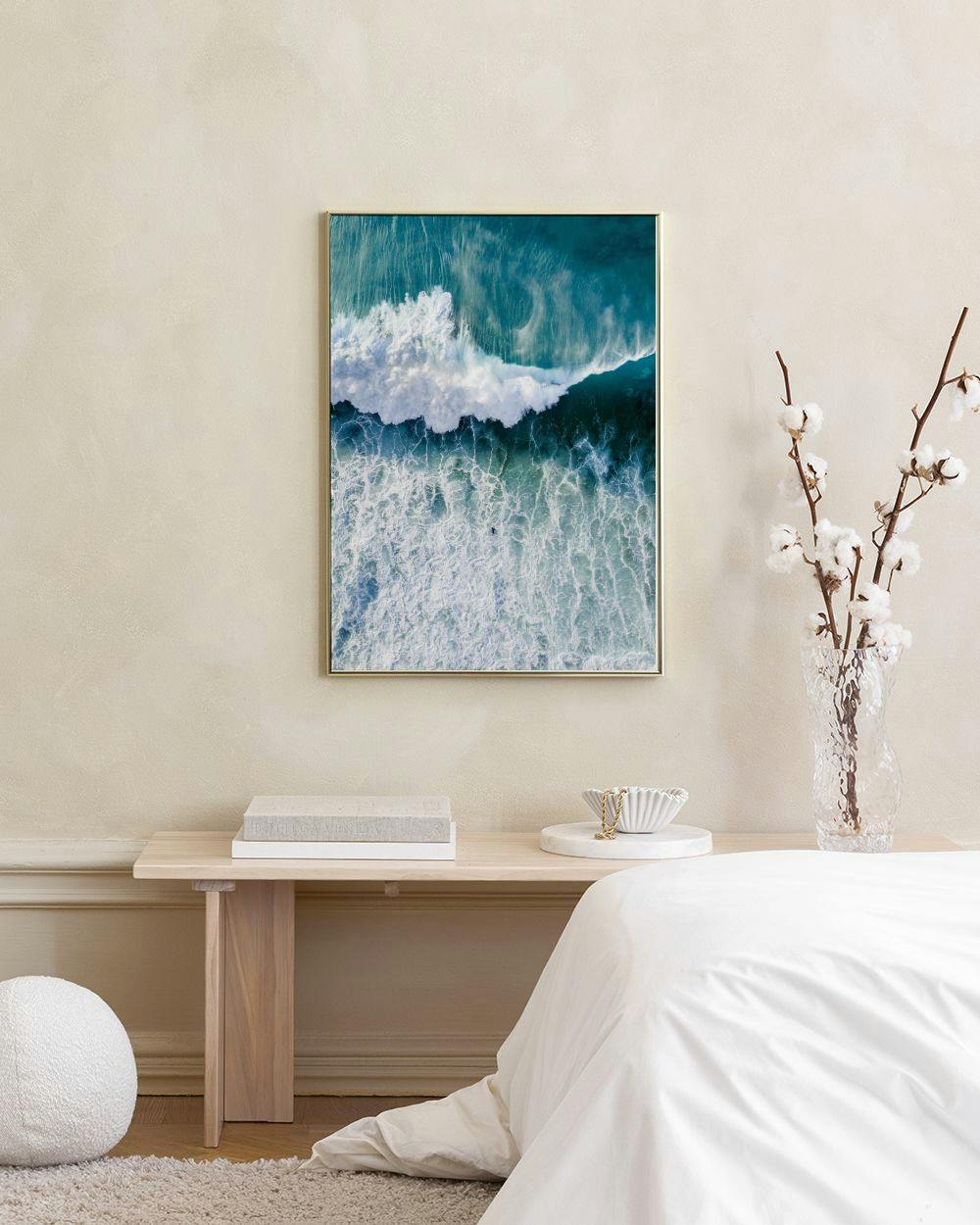 Affiche dune vague océanique turquoise et blanche, suspendue au-dessus dun meuble blanc avec un vase et une chaise bleue.