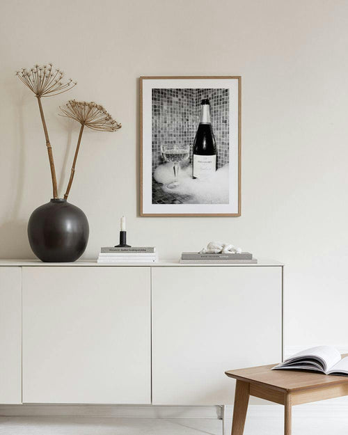 Affiche noire et blanche dune bouteille de champagne et dune coupe dans un bain moussant, affichée dans un salon moderne.