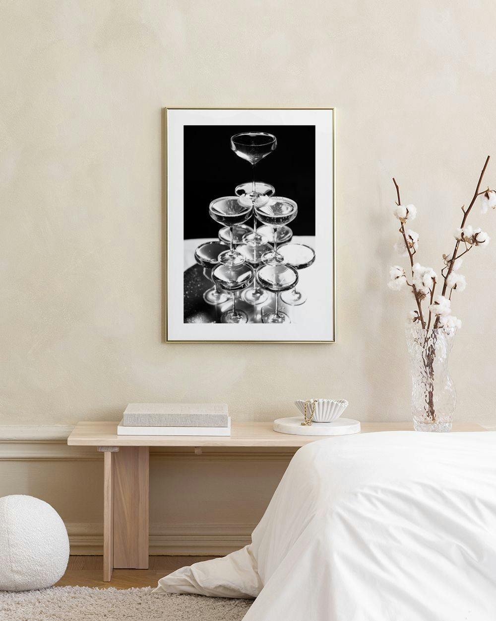 Affiche noire et blanche dune pyramide de coupes de champagne, accrochée sur un mur vert foncé, près dun tabouret en velours.