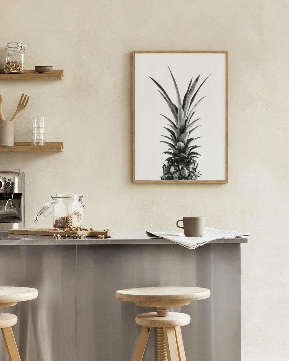 Affiche ananas noir et blanc, suspendue au-dessus dune table avec livre et chaise dans un intérieur moderne.