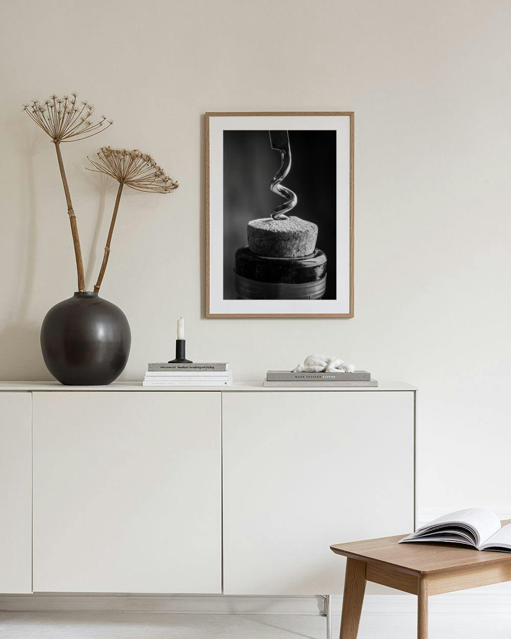 Affiche en noir et blanc dun tire-bouchon dans un bouchon de liège, suspendue au-dessus dune table avec un livre et une bougie.
