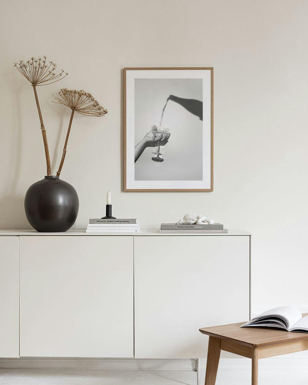 Affiche en noir et blanc dune main tenant un verre, avec lombre dune bouteille versant dedans. Accrochée au-dessus dun meuble av