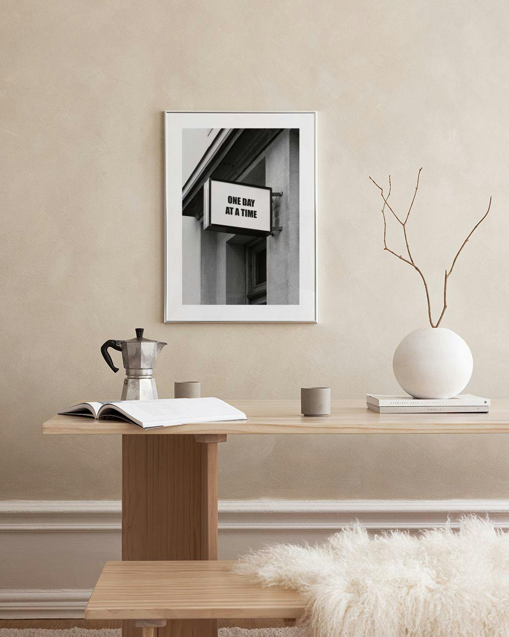 Affiche noire et blanche dune enseigne ONE DAY AT A TIME sur un mur, accrochée au-dessus dune table basse en marbre.