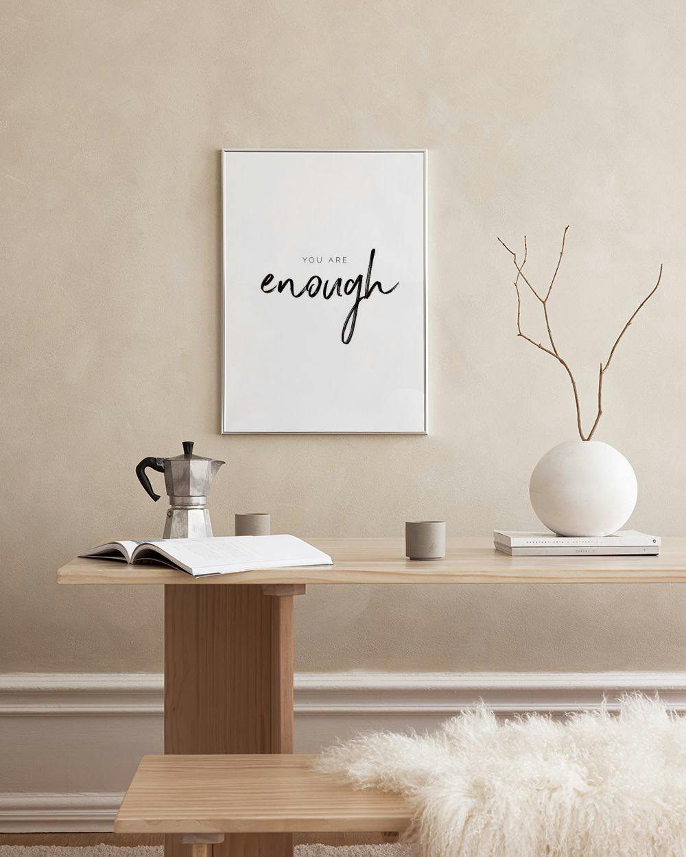 Affiche murale You Are Enough en écriture noire, suspendue au-dessus dune table basse en bois avec des vases roses.