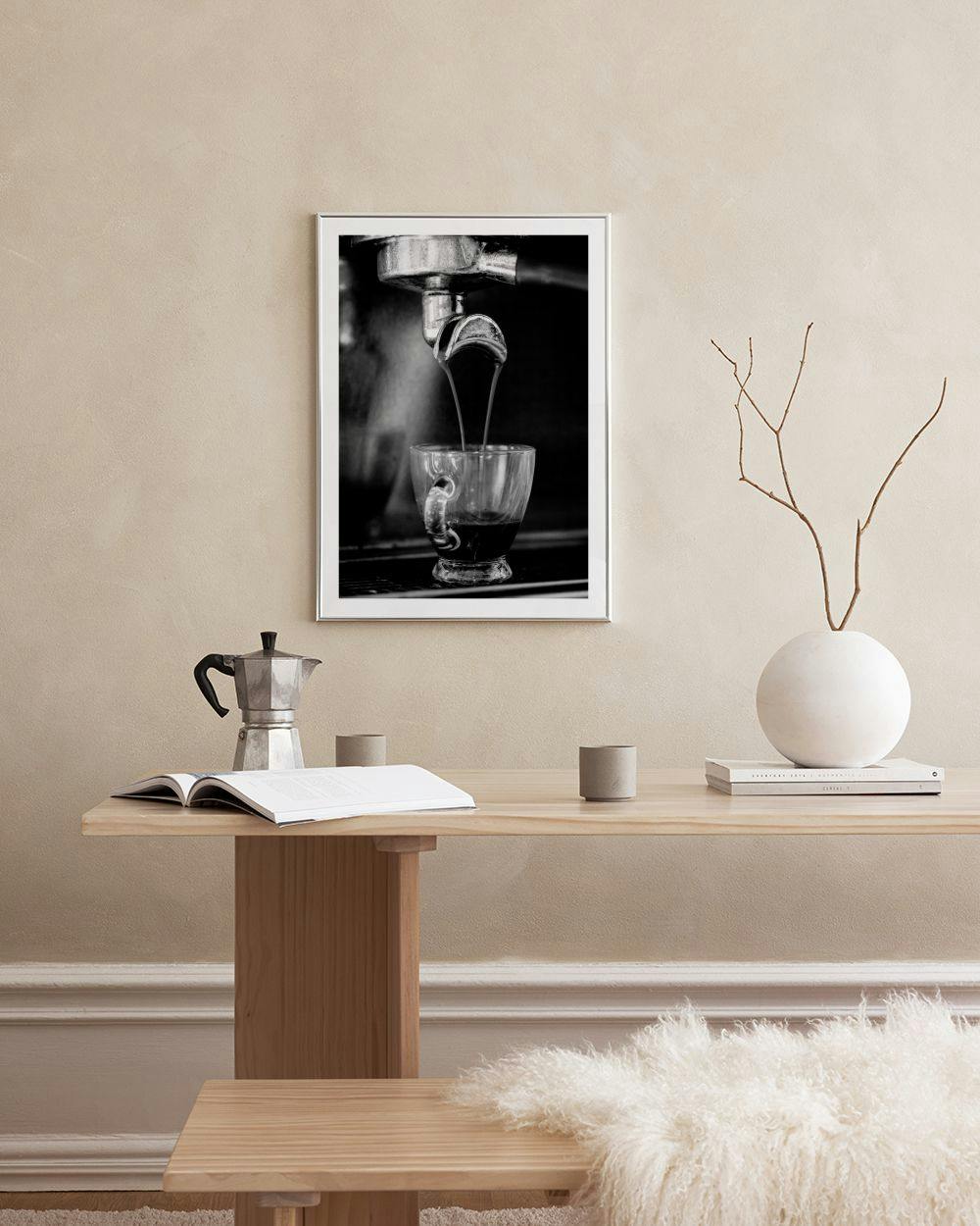 Affiche en noir et blanc dun café coulant dans une tasse, accrochée au-dessus dune table avec un livre et une chaise.