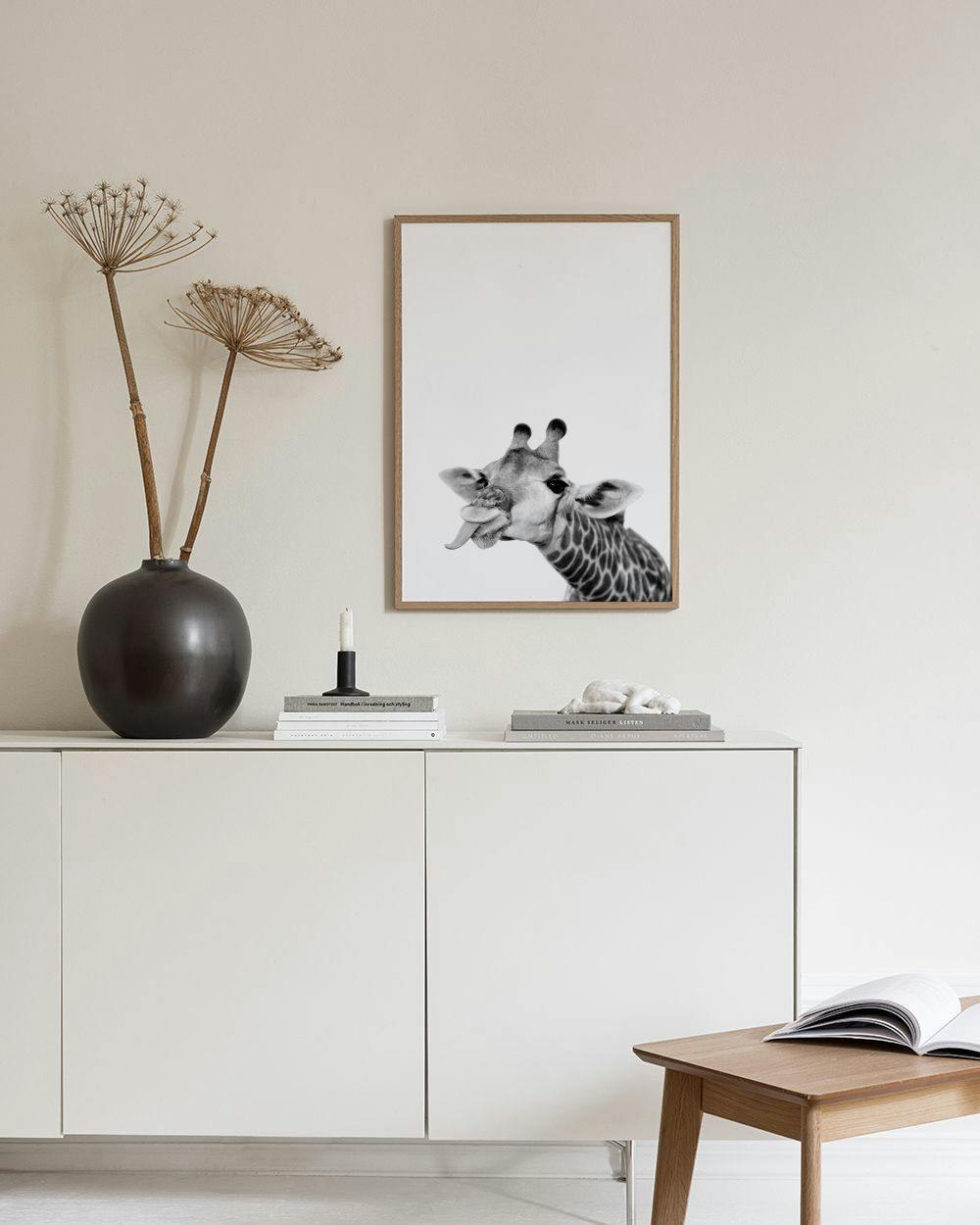 Affiche noire et blanche dune girafe tirant la langue, exposée sur un buffet blanc dans une pièce lumineuse.