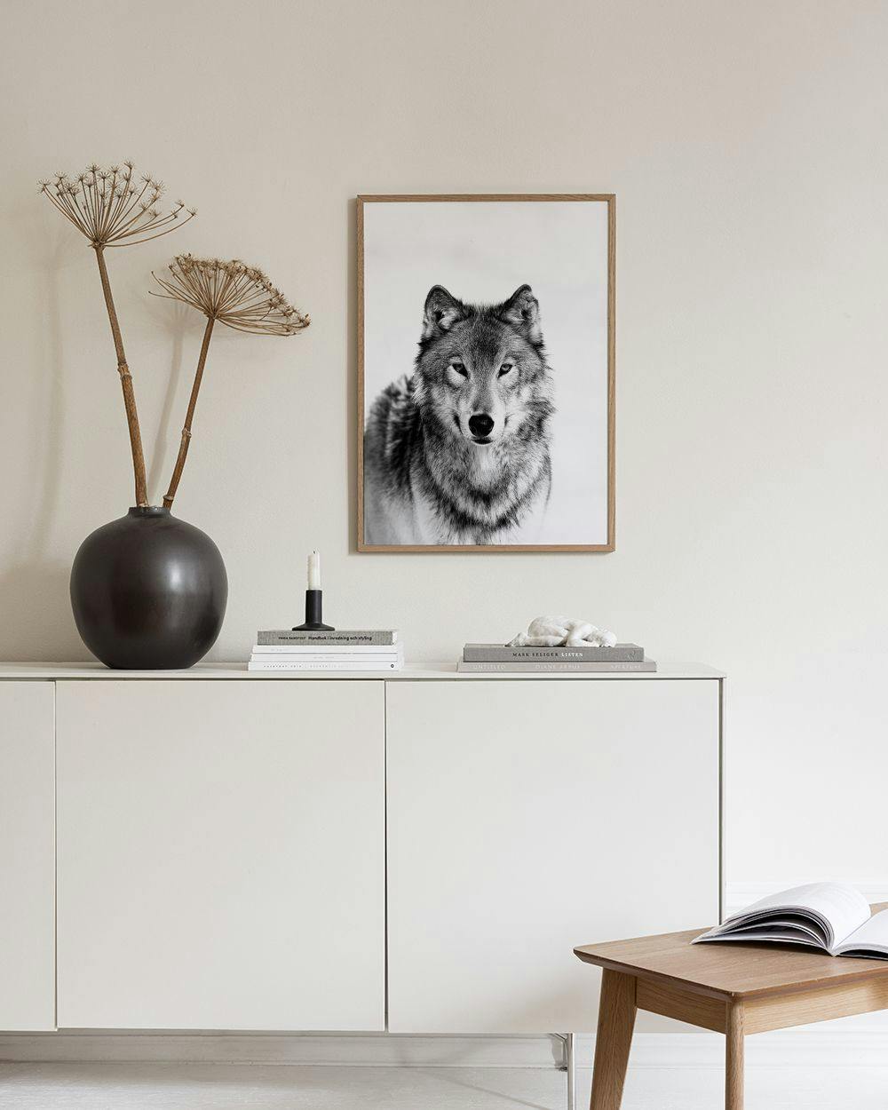 Affiche dun loup gris en noir et blanc, accrochée au mur blanc au-dessus dun tabouret en liège.