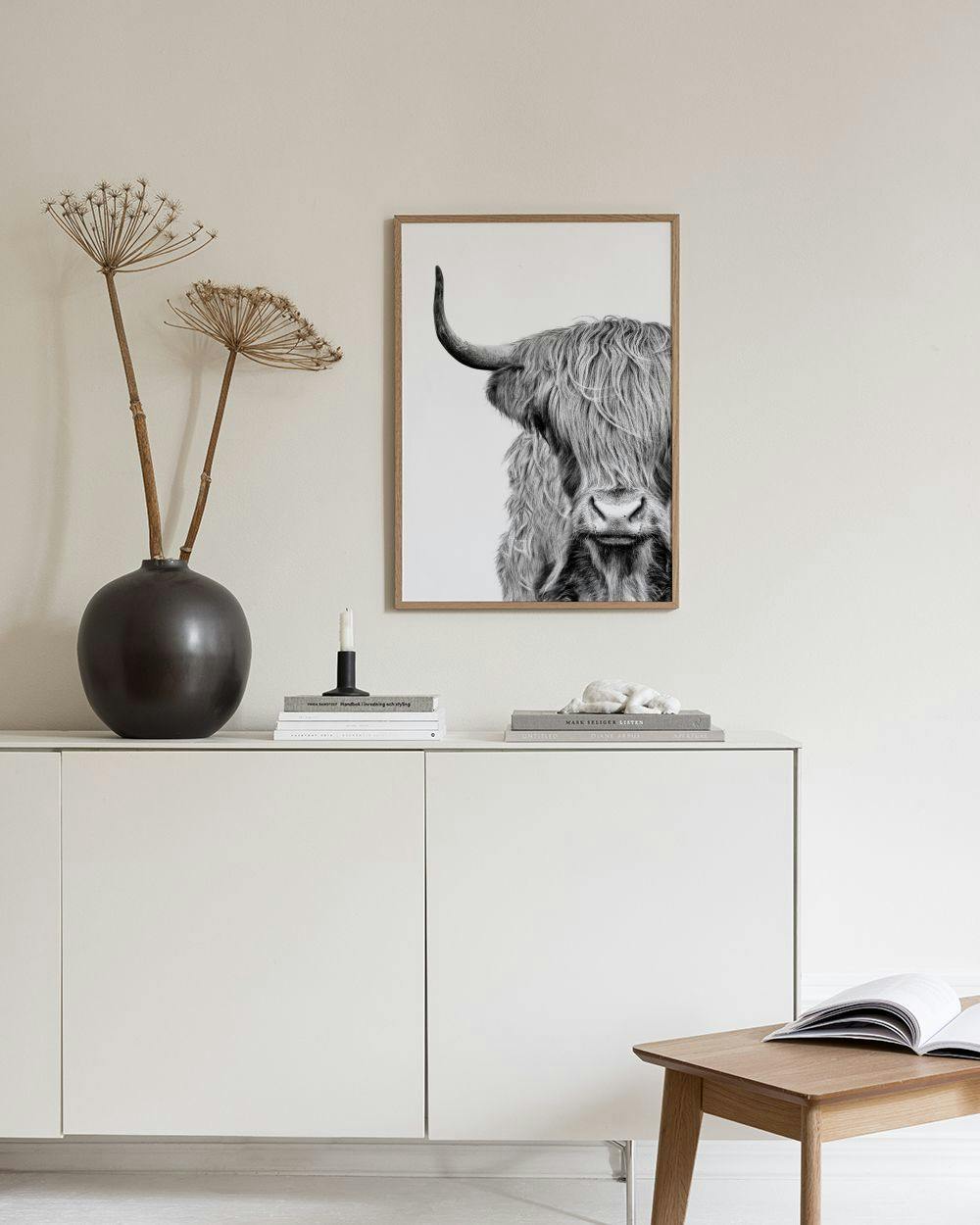 Affiche noire et blanche dune vache des Highlands, suspendue au-dessus dun tabouret en liège avec des livres.