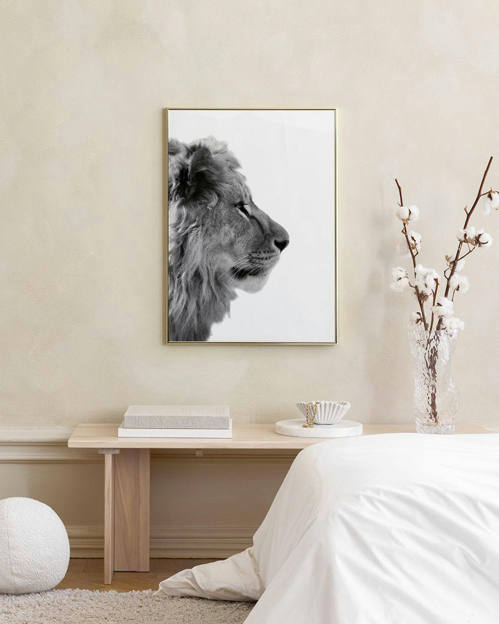 Affiche noir et blanc dun lion de profil sur un mur gris, avec un pouf rose et une table basse en verre.