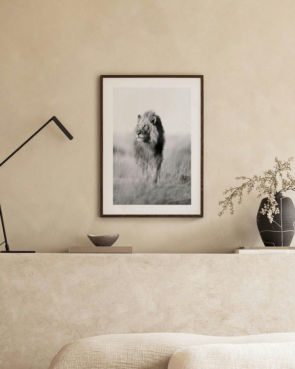 Affiche dun lion marchant en noir et blanc, accrochée au-dessus dun meuble blanc avec des livres et des vases.