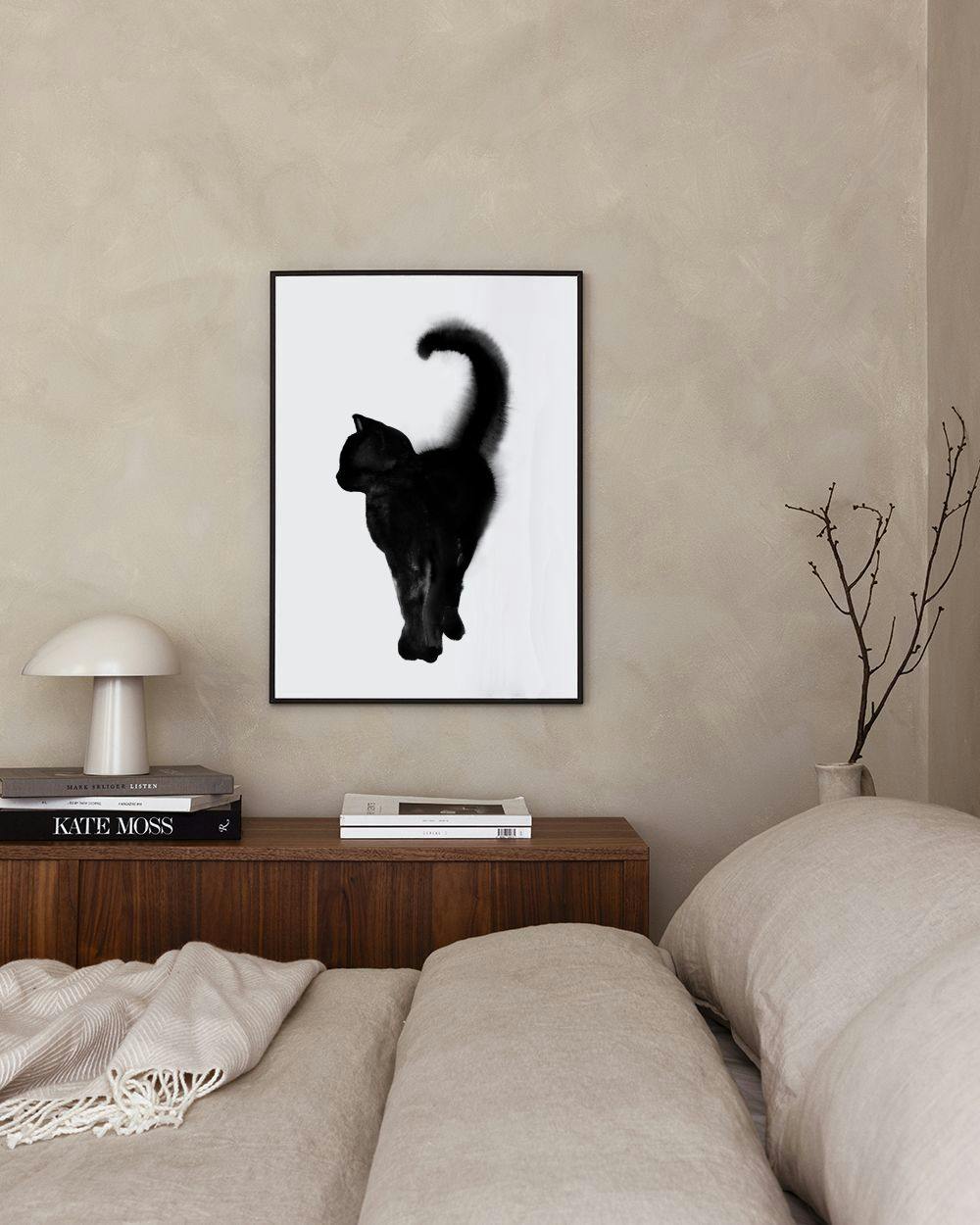 Affiche dun chat noir stylisé, accrochée au mur au-dessus dune table en bois clair avec des livres.