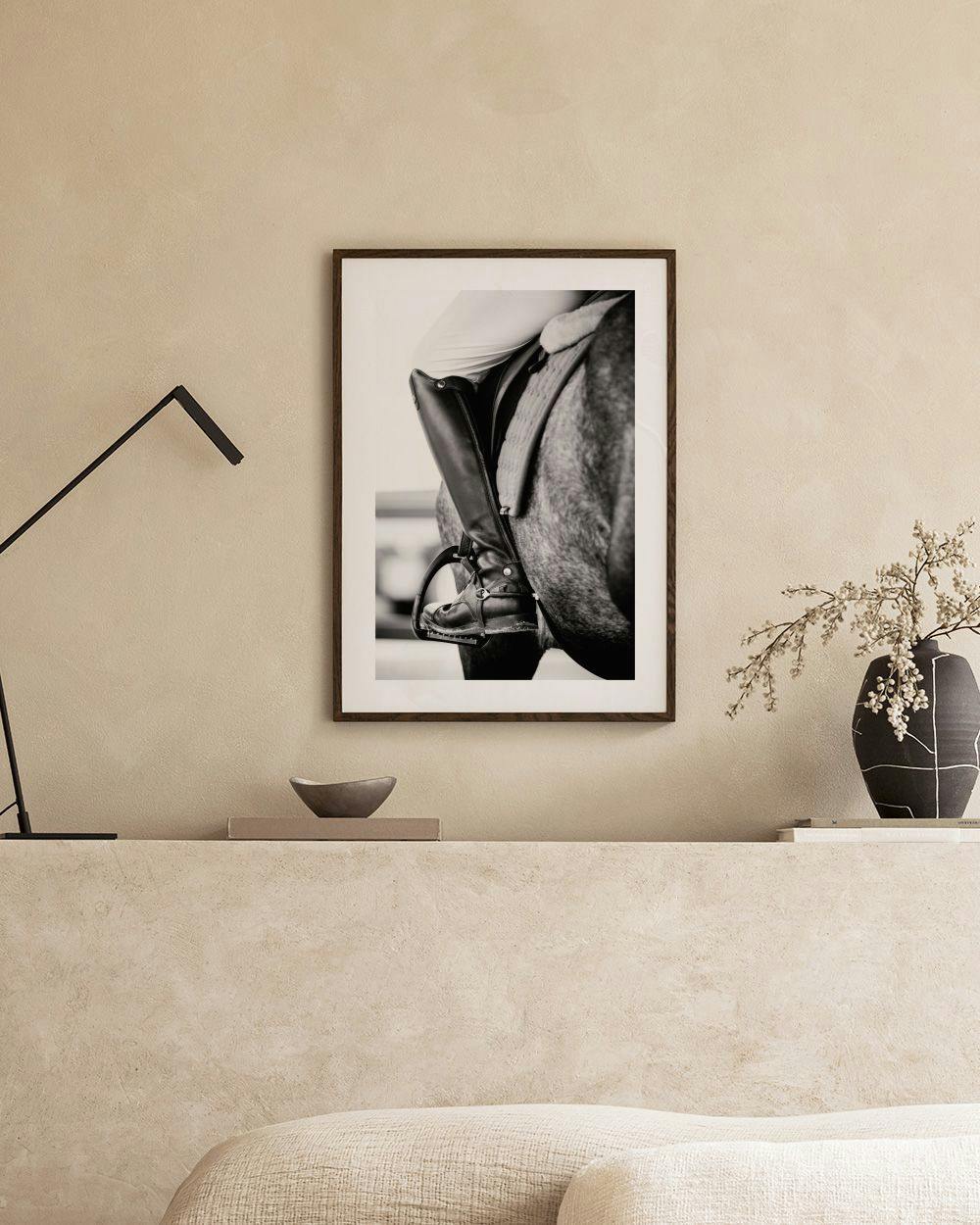 Affiche noir et blanc d’une botte déquitation et dune selle sur un cheval, au-dessus dun tabouret avec des livres.