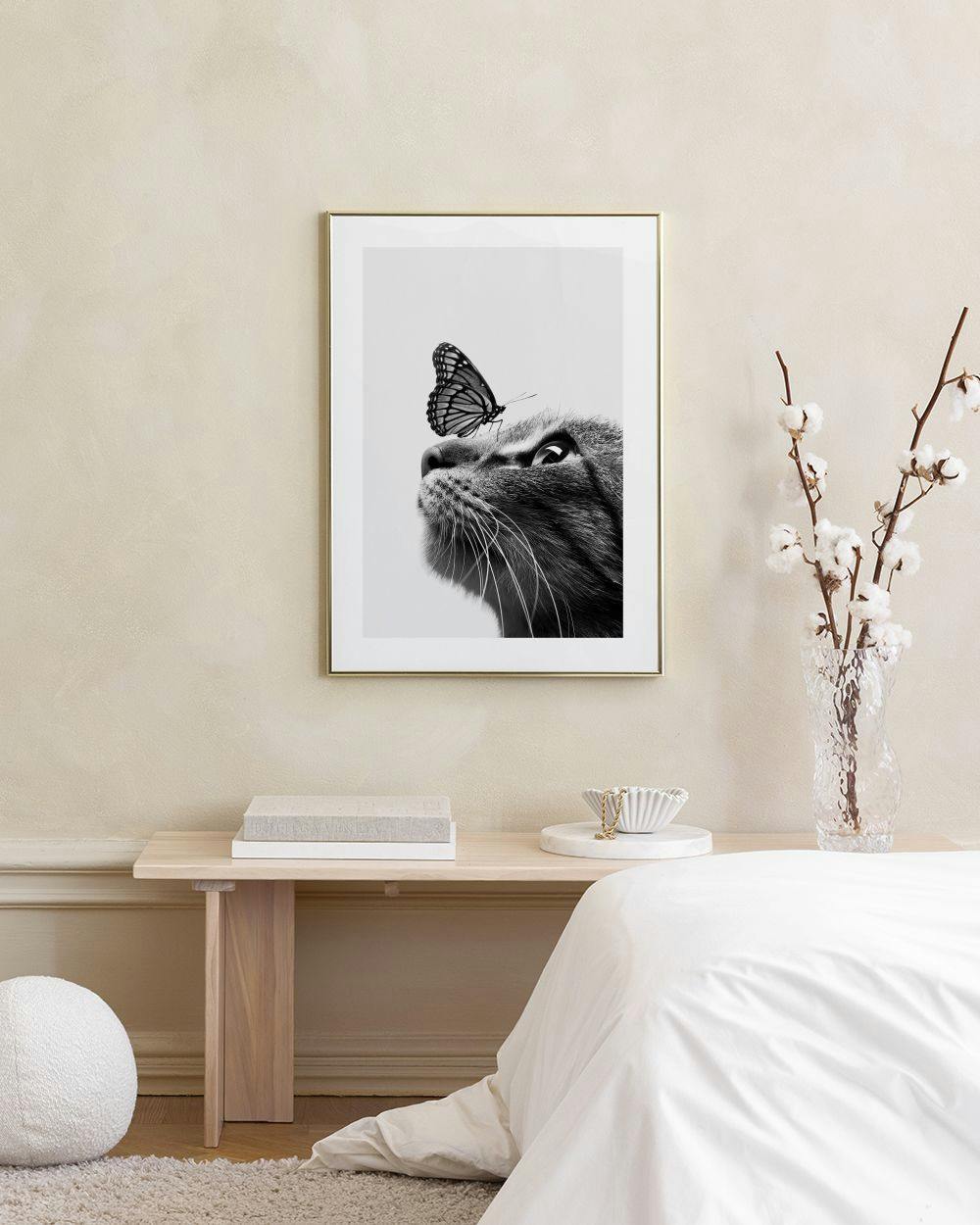 Affiche noir et blanc dun chat au regard curieux avec un papillon sur le nez, accrochée au-dessus dun banc en rotin.