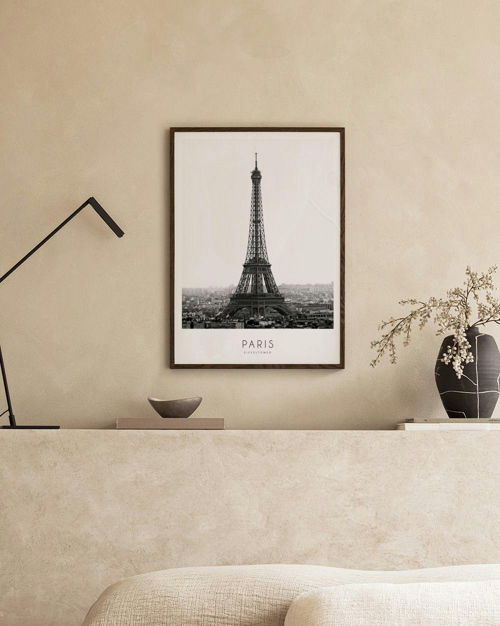 Affiche noir et blanc de la Tour Eiffel sur un meuble blanc, avec bougeoirs, vases et plante verte, fond bleu nuit.