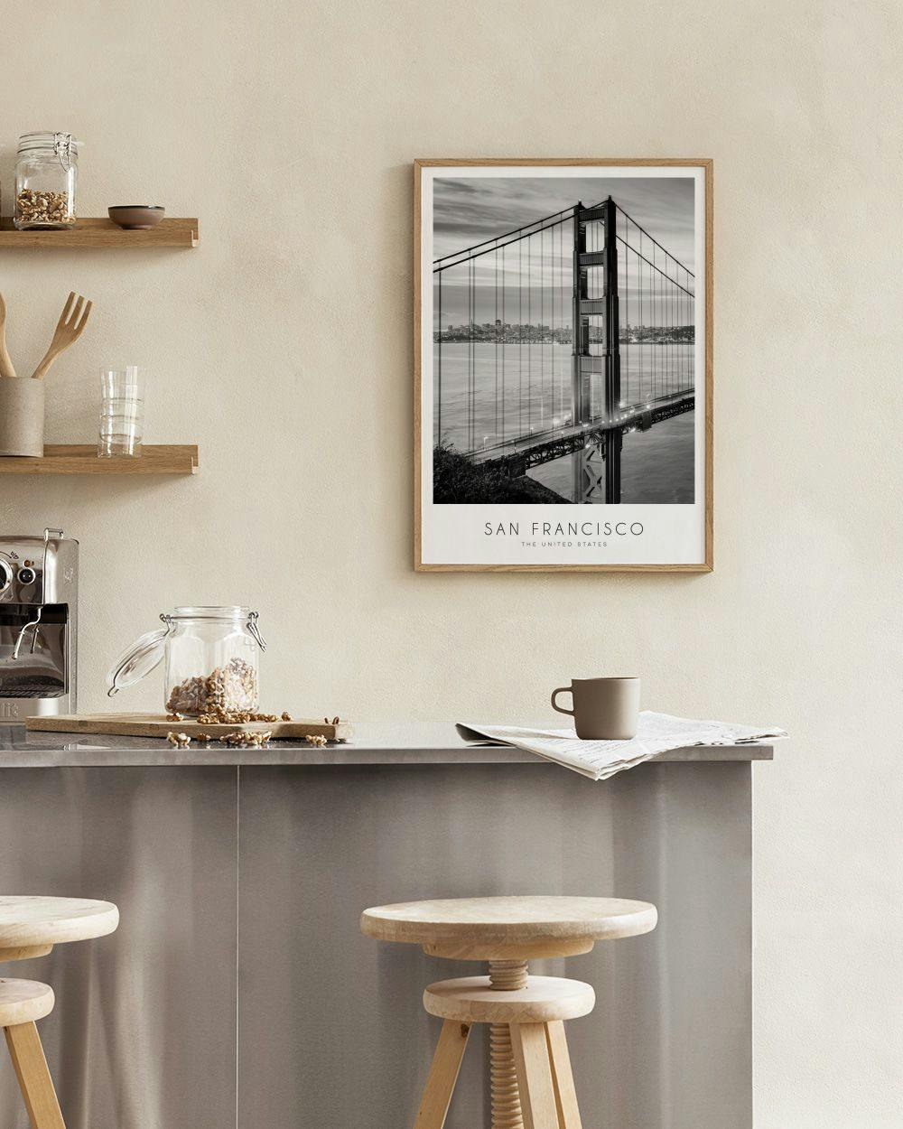 Affiche du Golden Gate Bridge en noir et blanc, accrochée au mur au-dessus dune étagère noire avec des livres et une cloche en v