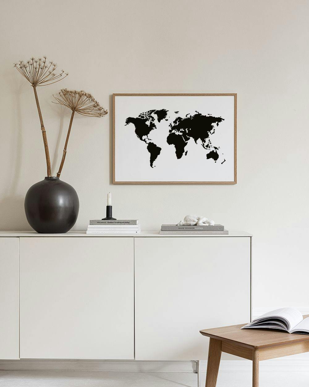 Affiche carte du monde noire sur fond blanc, accrochée au-dessus dune table basse dans un salon moderne.