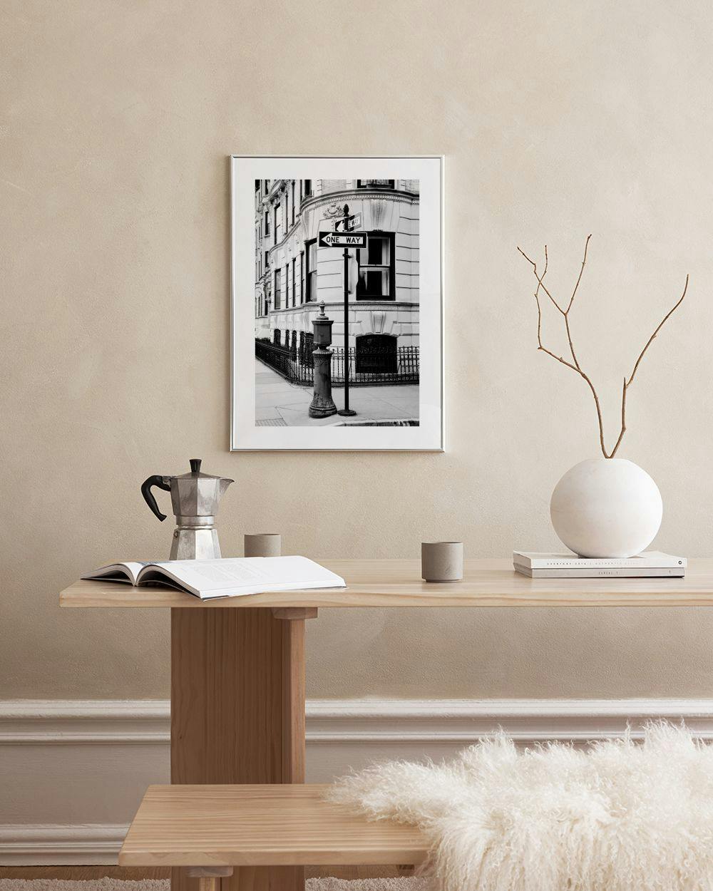 Affiche en noir et blanc dun panneau One Way dans une rue de ville, accrochée au-dessus dun meuble blanc.