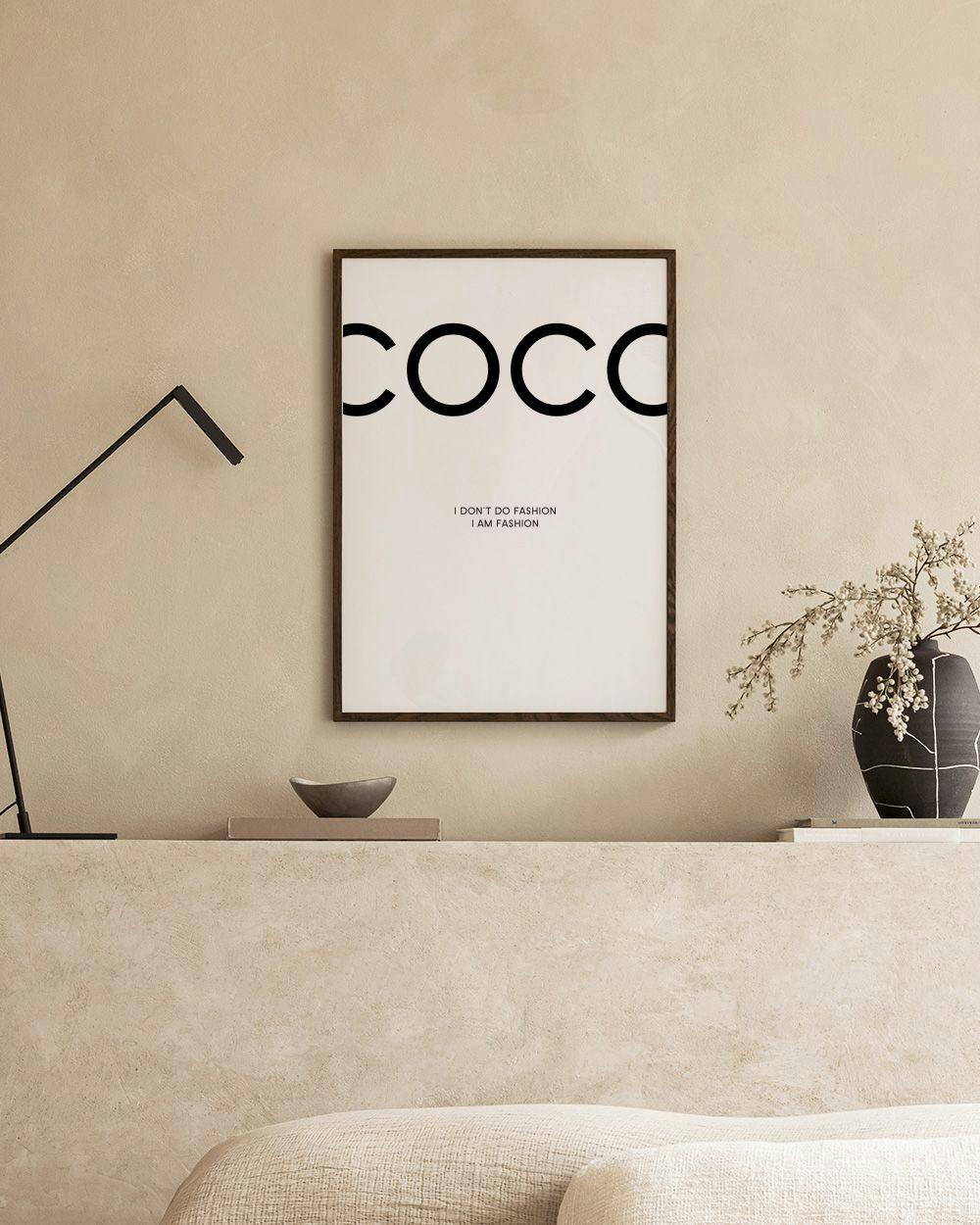 Affiche avec le mot COCO en noir, et I DONT DO FASHION I AM FASHION sur fond blanc, au-dessus dune étagère noire.