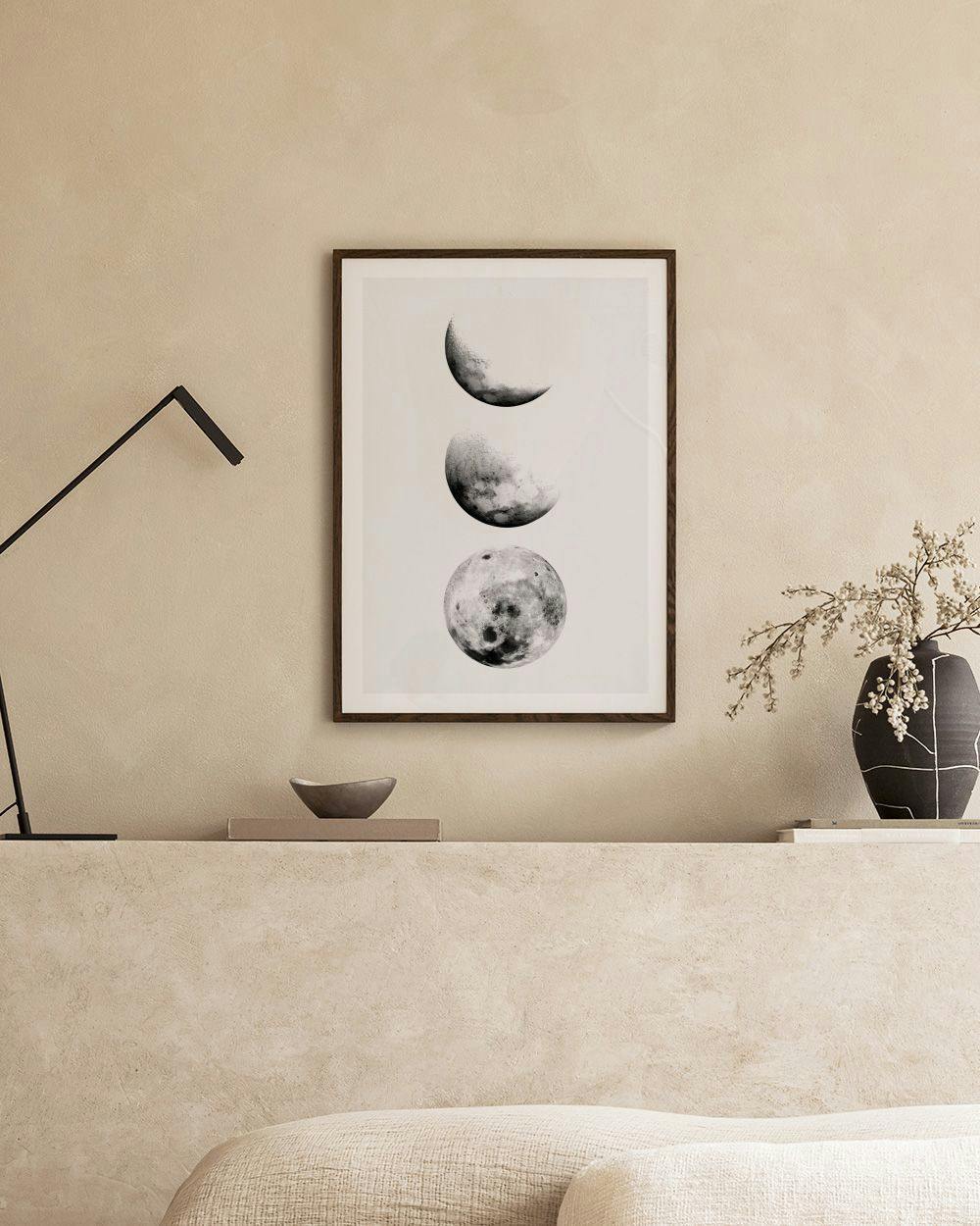 Affiche noire et blanche des phases de la lune, posée sur une étagère avec un cactus et un chandelier.