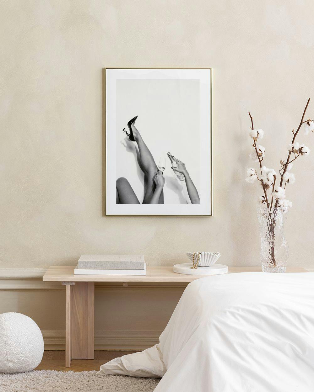 Affiche en noir et blanc de jambes féminines avec un verre et une bouteille, accrochée au-dessus dun canapé rose.