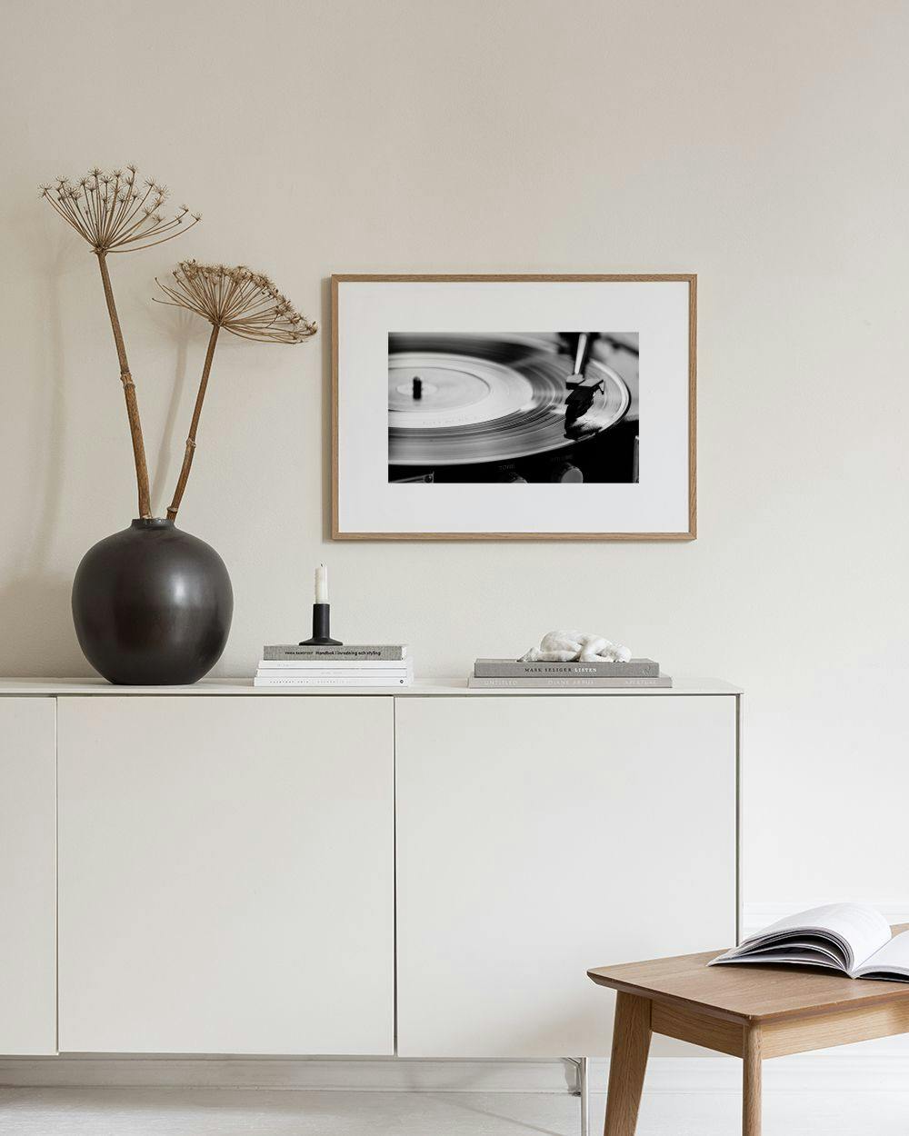 Affiche noir et blanc d’un vinyle tournant, suspendue au-dessus d’une console noire avec une plante et des livres.