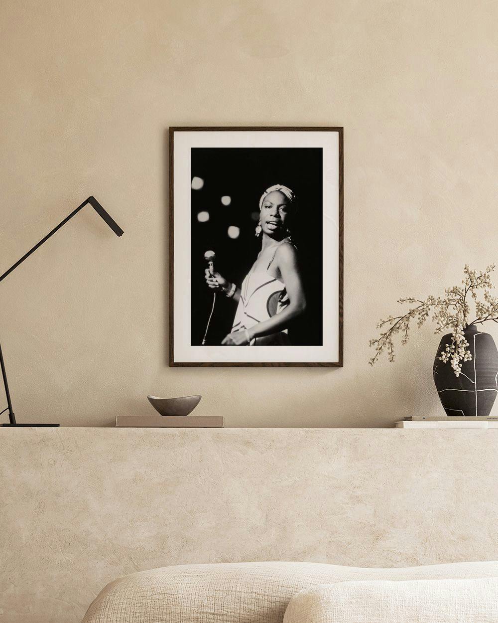Affiche en noir et blanc de Nina Simone chantant, affichée au-dessus dun banc en béton avec des vases décoratifs.
