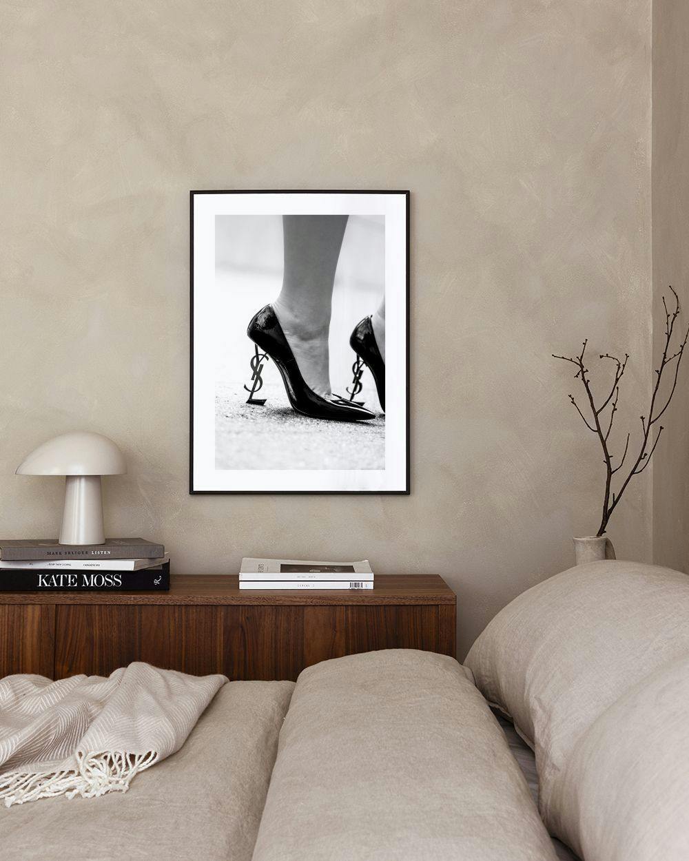 Affiche en noir et blanc de talons aiguilles avec le logo YSL en guise de talon, affichée dans un salon moderne.