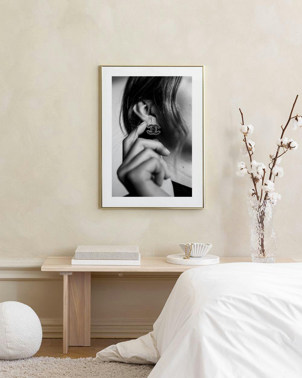 Affiche en noir et blanc dune femme mettant une boucle doreille Chanel, affichée au-dessus dune table avec des vases.