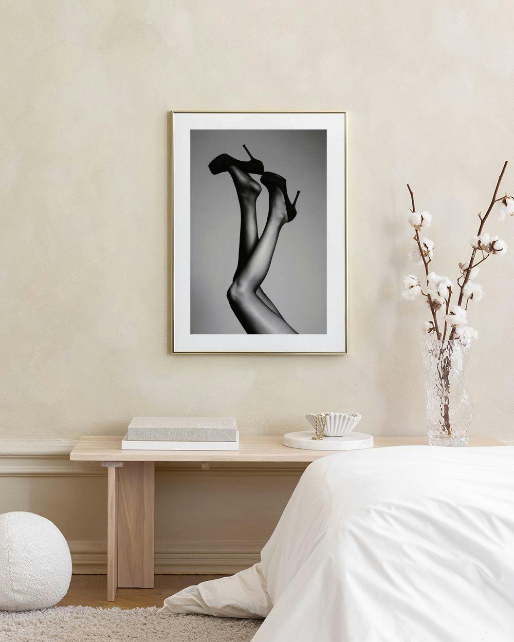 Affiche en noir et blanc de jambes féminines en talons hauts, suspendue au-dessus dun buffet gris.