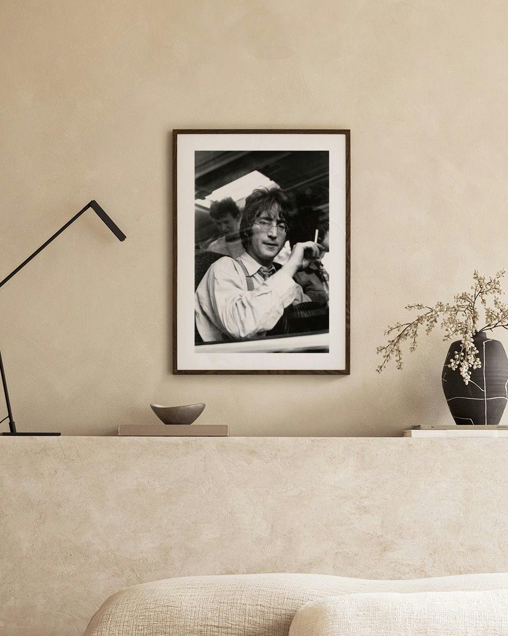 Affiche noir et blanc de John Lennon, lunettes rondes et cigarette, exposée dans un salon moderne.