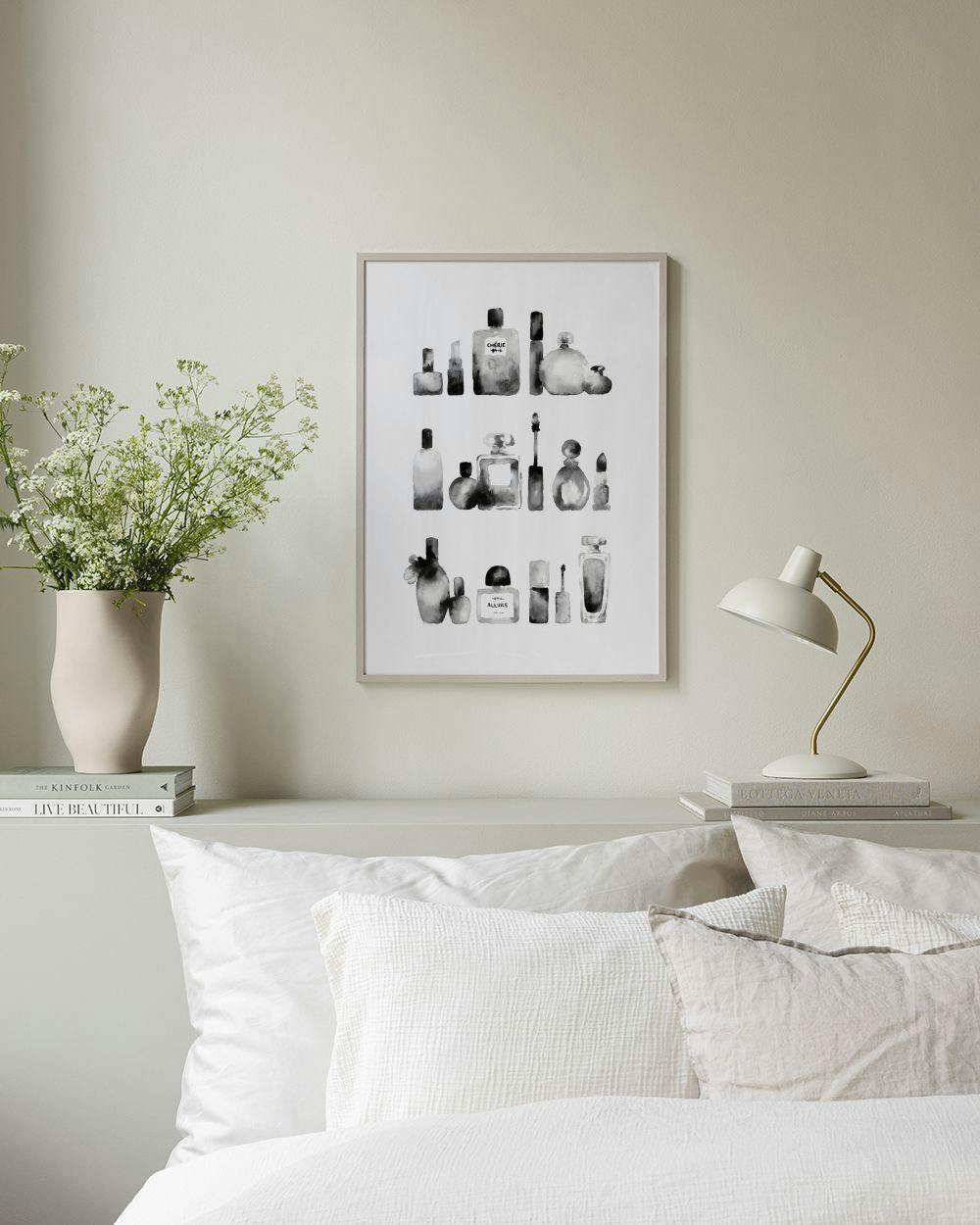 Affiche noire et blanche de flacons de parfum et cosmétiques, exposée au-dessus dun meuble blanc avec un vase et un livre dans u
