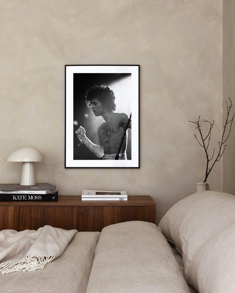 Affiche noir et blanc de Prince sur scène, accrochée dans une pièce lumineuse au-dessus dun meuble blanc avec un vase et un tabo