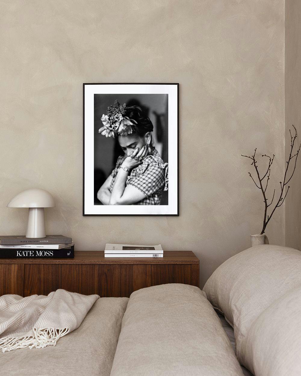Affiche noir et blanc de Frida Kahlo, la tête baissée, posant sa main sur sa joue, exposée dans un salon moderne.