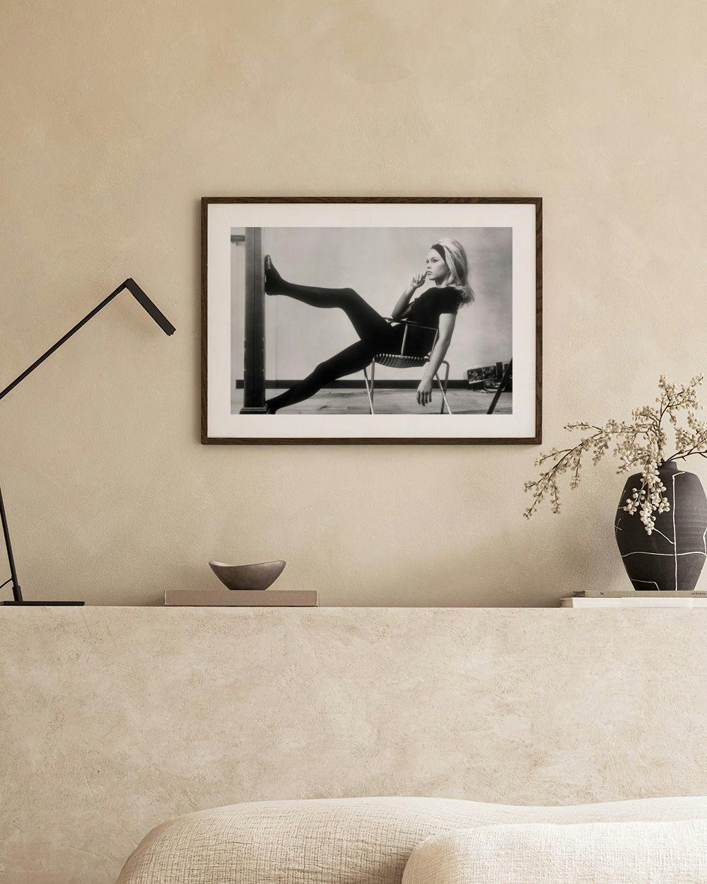 Affiche noir et blanc de Brigitte Bardot posant sur une chaise, affichée dans un salon moderne.