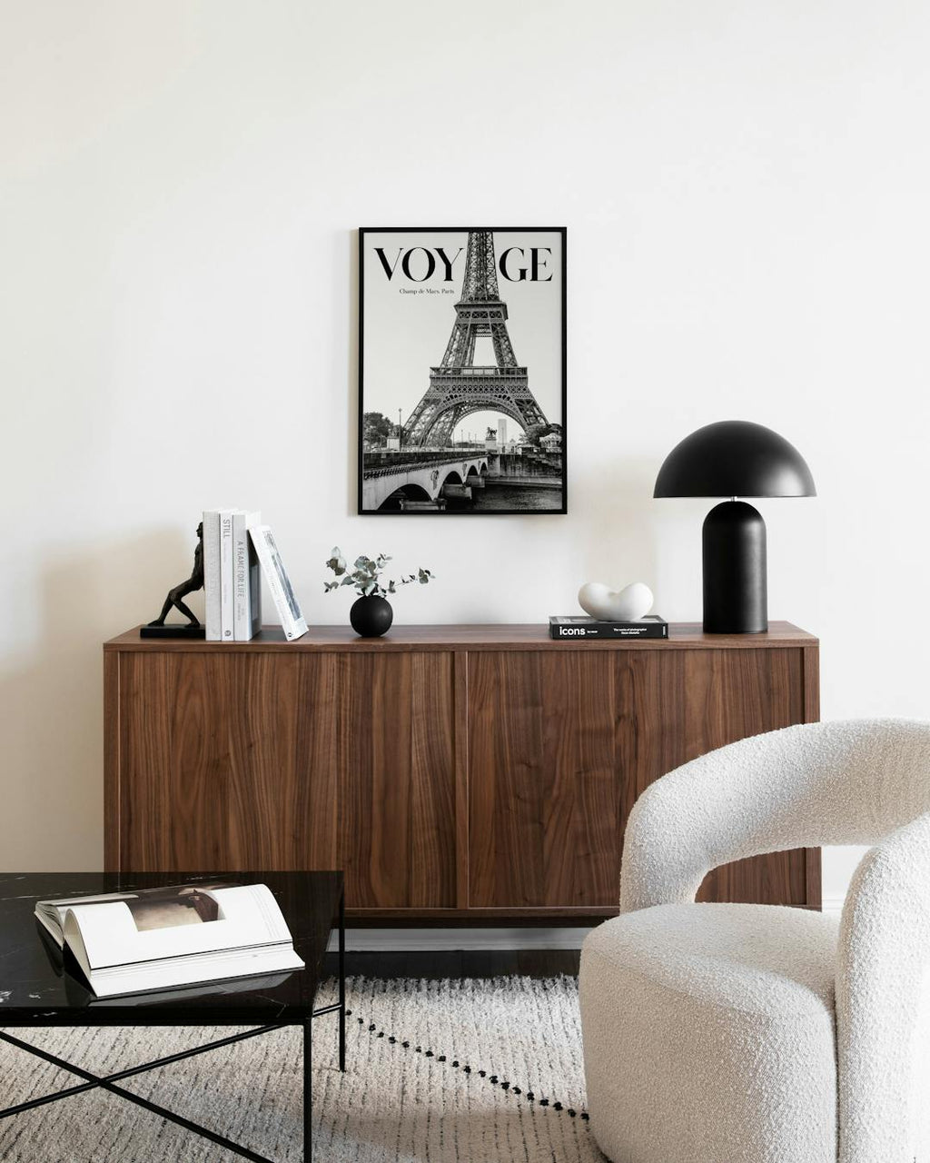 Affiche noir et blanc de la Tour Eiffel avec le mot VOYAGE, accrochée au-dessus dun buffet en bois.