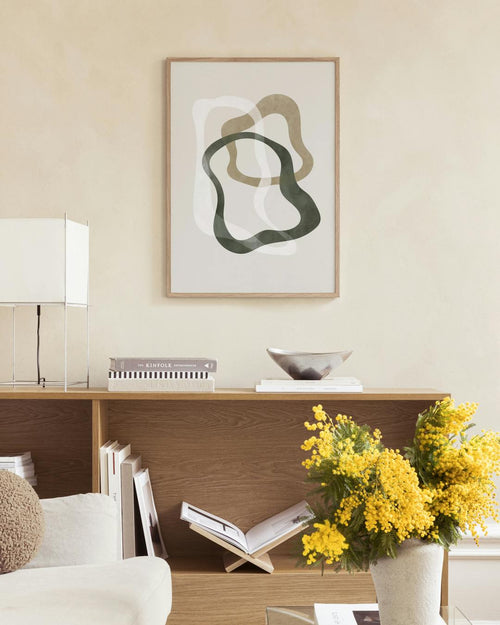 Affiche abstraite aux formes organiques vertes, beiges et blanches, suspendue dans une pièce aux murs gris.