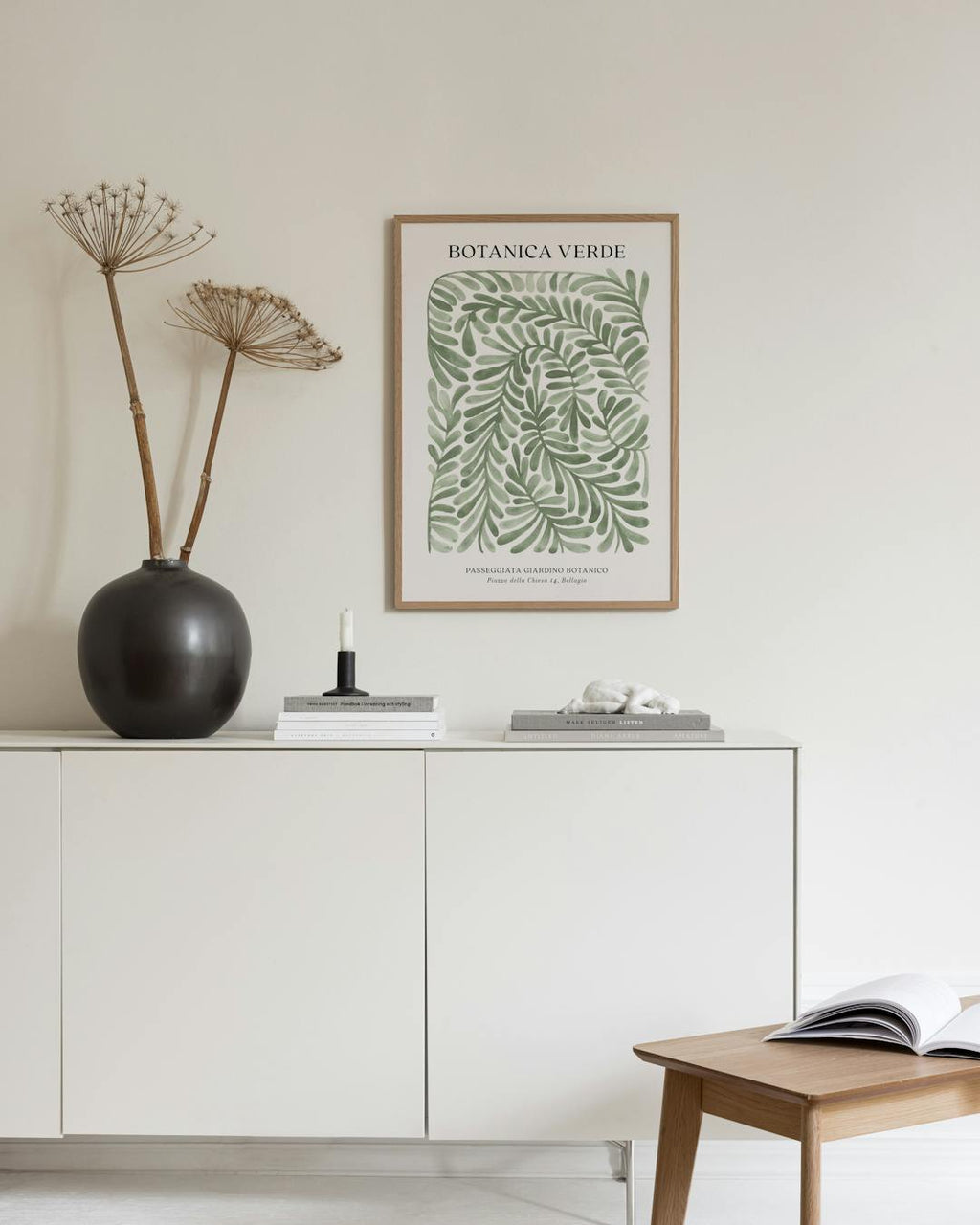 Affiche Botanica Verde avec motifs de feuilles vertes, affichée au-dessus dun meuble blanc dans un salon moderne.
